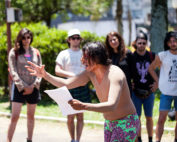 Fernanda Silva aparece em destaque lendo e se movimentando, Público observa de pé.